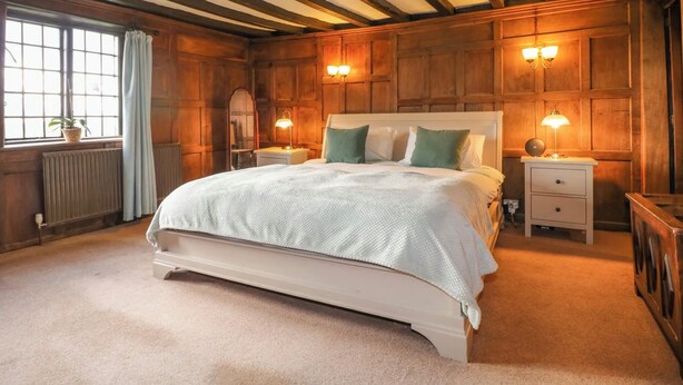 Une chambre à coucher avec un grand lit, un lambris en bois, deux tables de chevet avec des lampes, un radiateur et une fenêtre avec des rideaux.