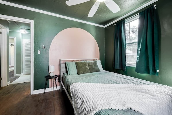 A bedroom with a bed, a round arch, a ceiling fan, and a window with curtains.