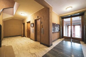 A hotel lobby with a marble floor, wooden doors, and a wall-mounted safe.