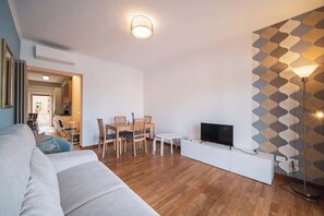 A modern living room with a sofa, dining table, chairs, a TV, and a patterned wall.
