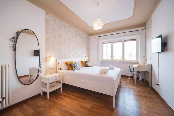 A bedroom with a bed, bedside table, chair, desk, and a TV.