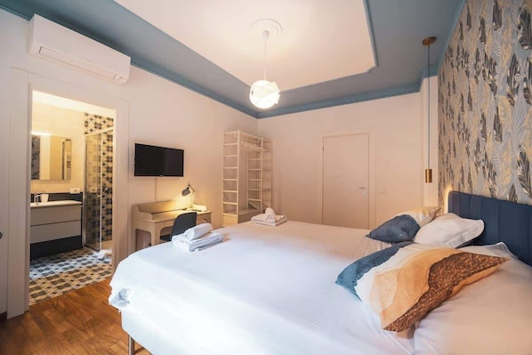 A bedroom with a bed, a desk, a wardrobe, and a television.
