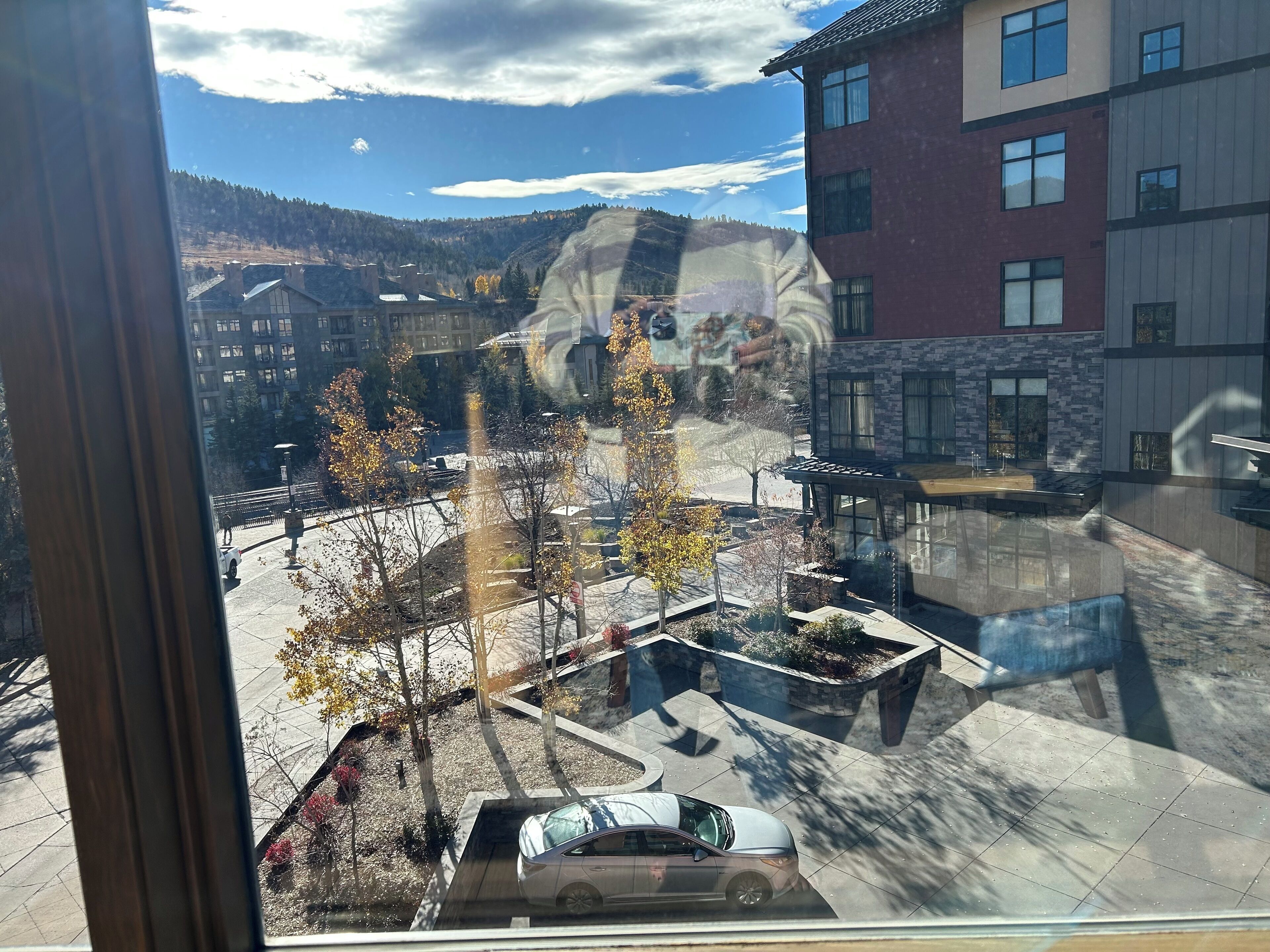 Vista desde una ventana sobre un estacionamiento con árboles y un edificio.