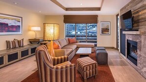A modern living room with a sectional sofa, a fireplace, a television, and a large window with a view of a snowy landscape. - Martin LutherKing ski break! Beaver Creek ski weekend. 2 bedroom condo (Avon)
