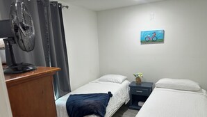 A bedroom with two beds, a desk, a chair, a fan, and a painting on the wall. - Cool Cottage near Ennis (Rice)