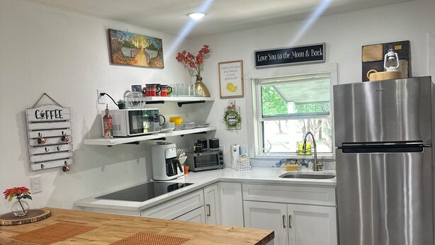 A kitchen with a wooden island, stainless steel appliances, white cabinets, and a black trash bin. - Cool Cottage near Ennis (Rice)