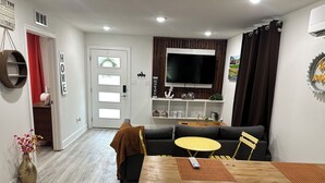 A living room with a sofa, a wooden dining table, a TV, and a door with frosted glass panels. - Cool Cottage near Ennis (Rice)