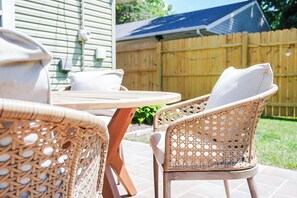 Gartenmöbel aus Rattan mit Kissen, ein runder Tisch und ein Holzzaun im Hintergrund.
