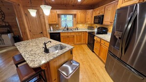 A kitchen with wooden cabinets, granite countertops, stainless steel appliances, and a window providing natural light. - Peaceful mountain cabin with amenties in Rumbling Bald resort, Lake Lure (Lake Lure)