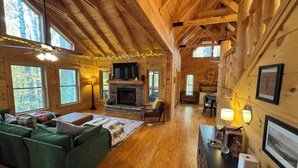 A log cabin interior with a fireplace, green sofa, wooden floors, and large windows. - Peaceful mountain cabin with amenties in Rumbling Bald resort, Lake Lure (Lake Lure)
