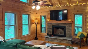 A cozy cabin interior with a green sofa, a fireplace, and large windows. - Peaceful mountain cabin with amenties in Rumbling Bald resort, Lake Lure (Lake Lure)