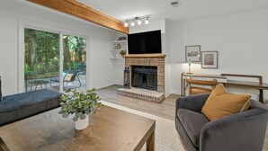 Ein Wohnzimmer mit Kamin, einer Couch, einem Couchtisch und einem Fernseher, der über dem Kamin angebracht ist.