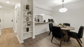 Eine moderne Küche mit weißen Schränken, einer eingebauten Kochinsel und einem Essbereich mit rundem Tisch und vier Stühlen.