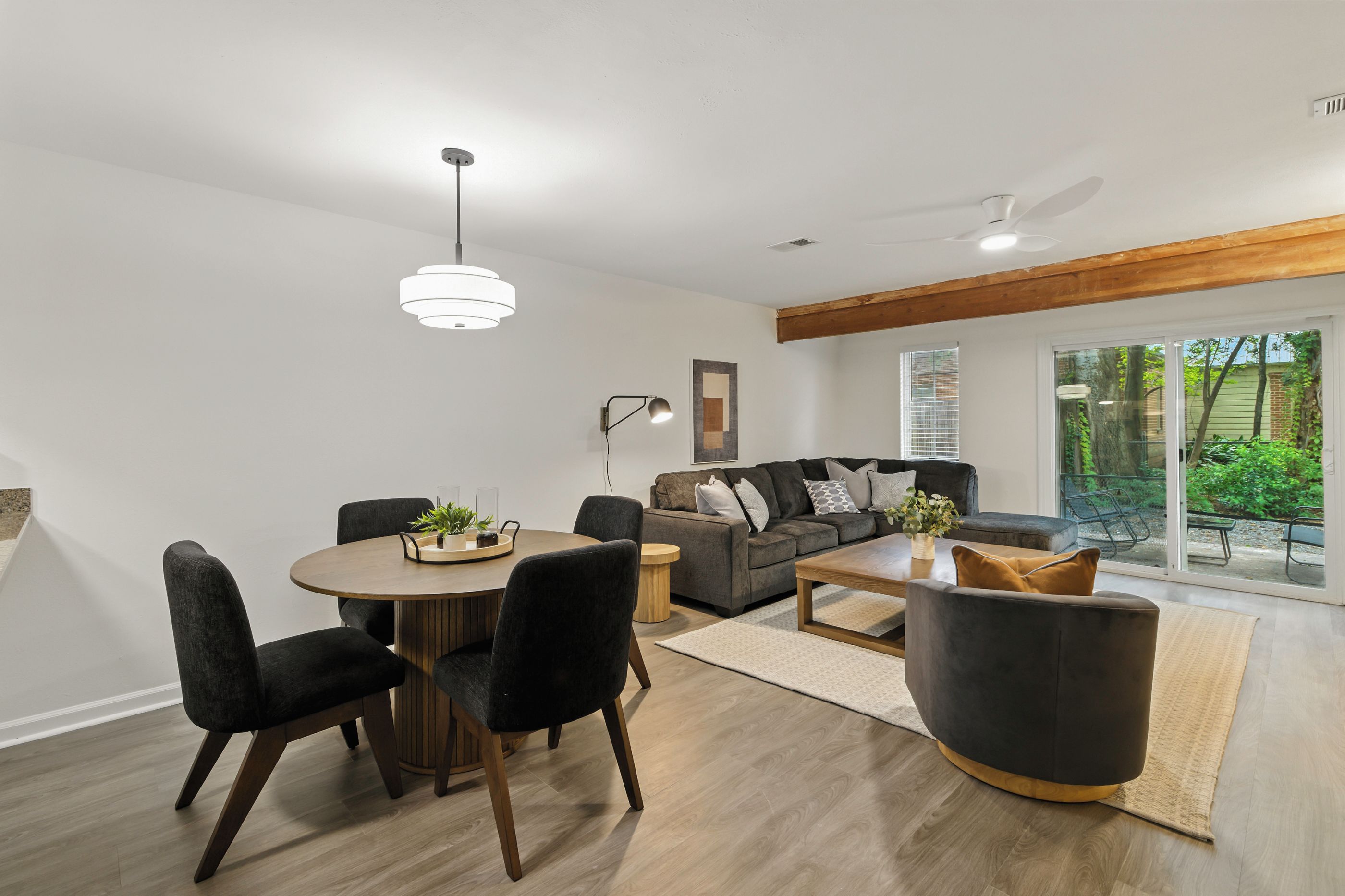 Een moderne woonkamer met een eethoek, een zithoek en een groot raam met uitzicht op groen.
