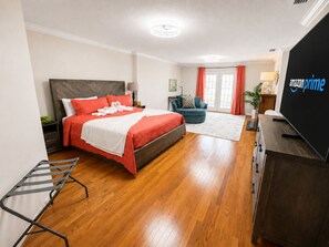 A modern hotel room with a large bed, a TV, a desk, and a seating area.