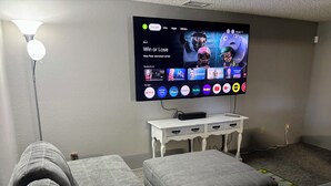 Une salle de cinéma maison avec un téléviseur à écran plat fixé au mur, des sièges rembourrés de couleur grise et une petite table d’appoint blanche.