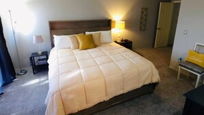 Une chambre d’hôtel avec un grand lit, une table de chevet avec une lampe, un banc et une armoire.