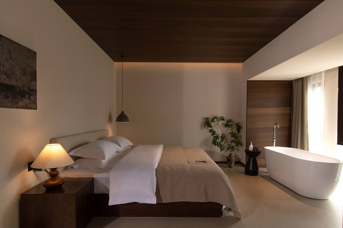 Un dormitorio moderno con una cama grande, una lámpara de noche y una bañera separada.