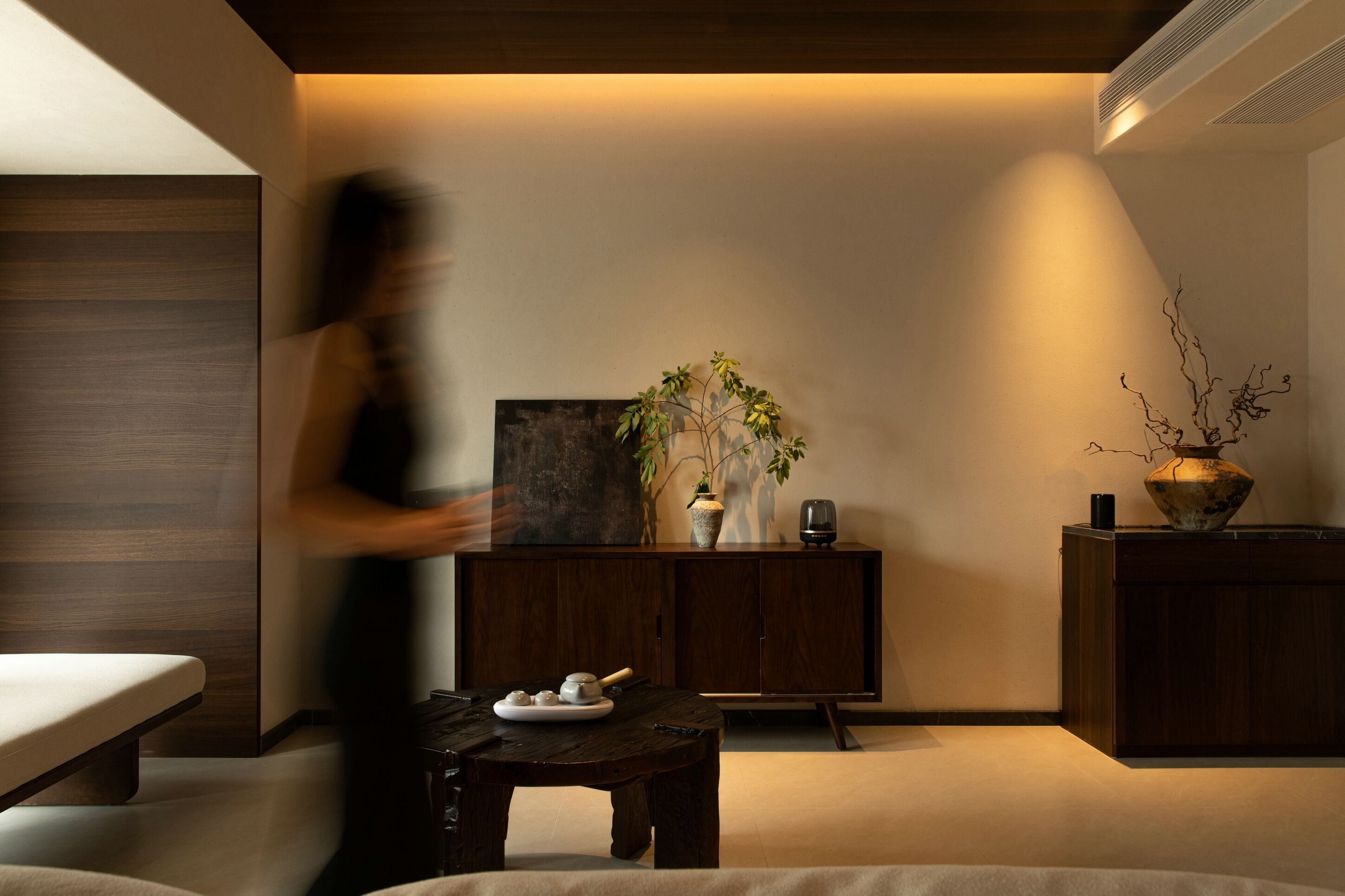 A modern room with a wooden cabinet, a table with teaware, and a vase with branches.
