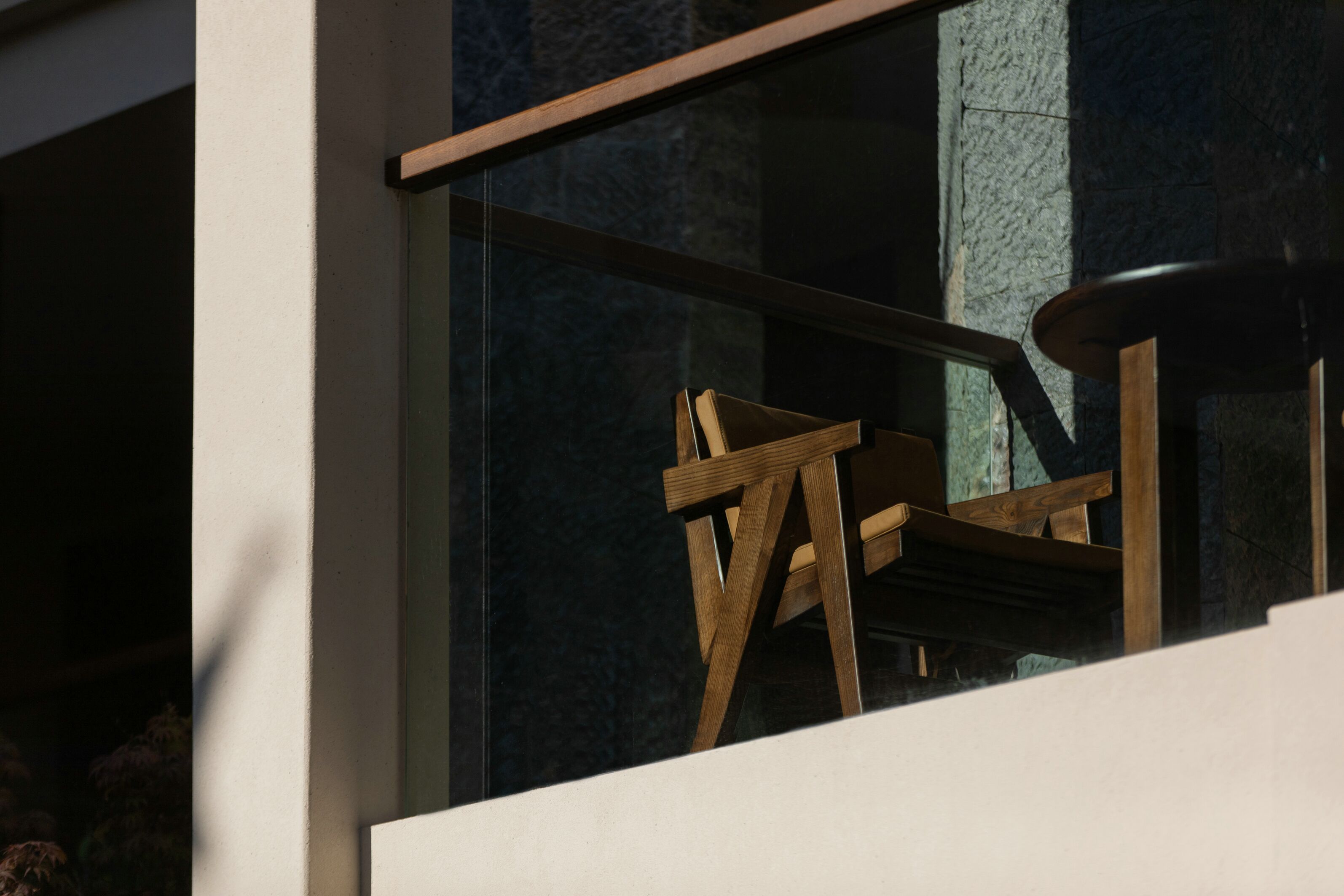 A modern building with a glass window and a wooden chair outside.