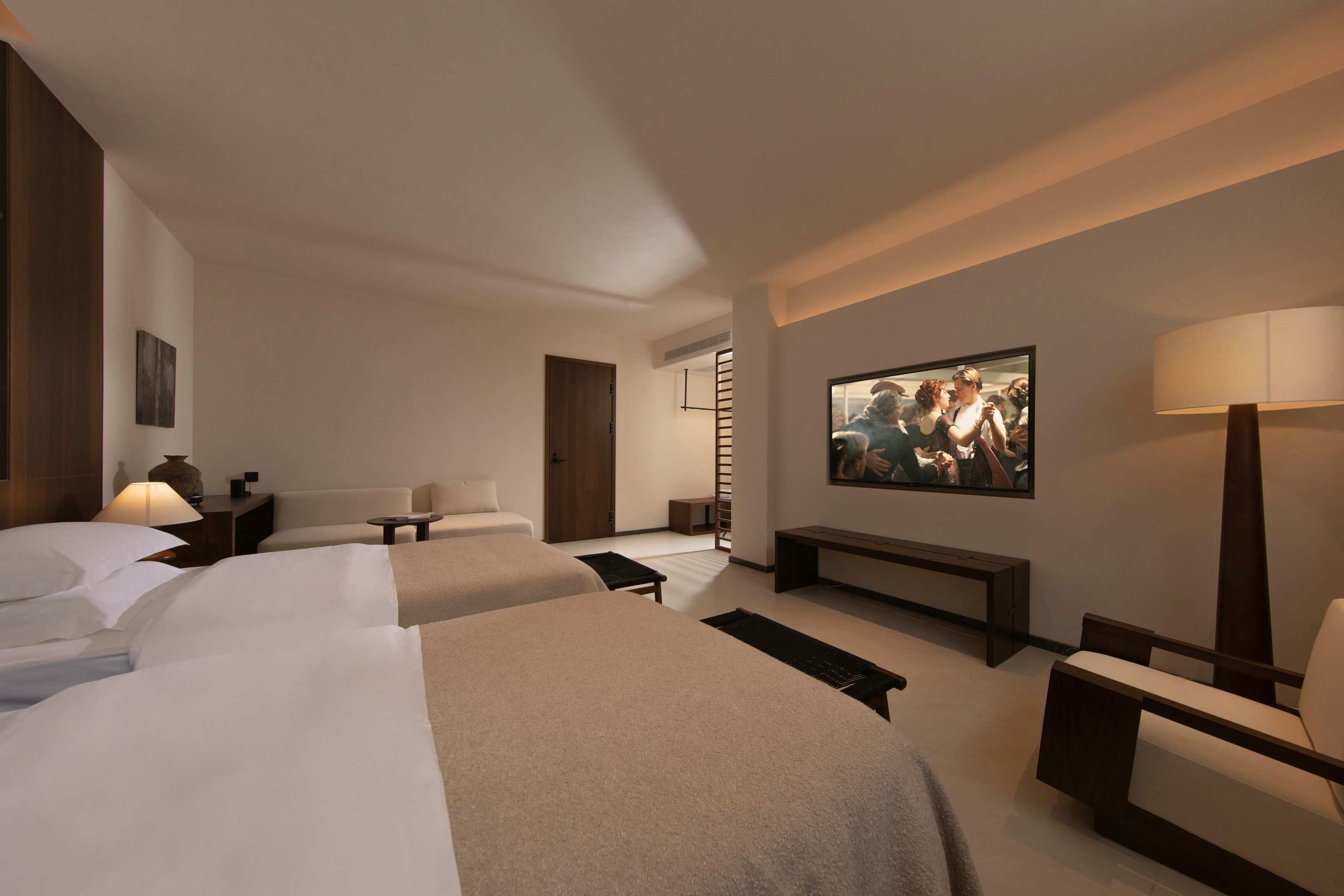 Una habitación de hotel moderna con dos camas, un sofá, un televisor y una lámpara.
