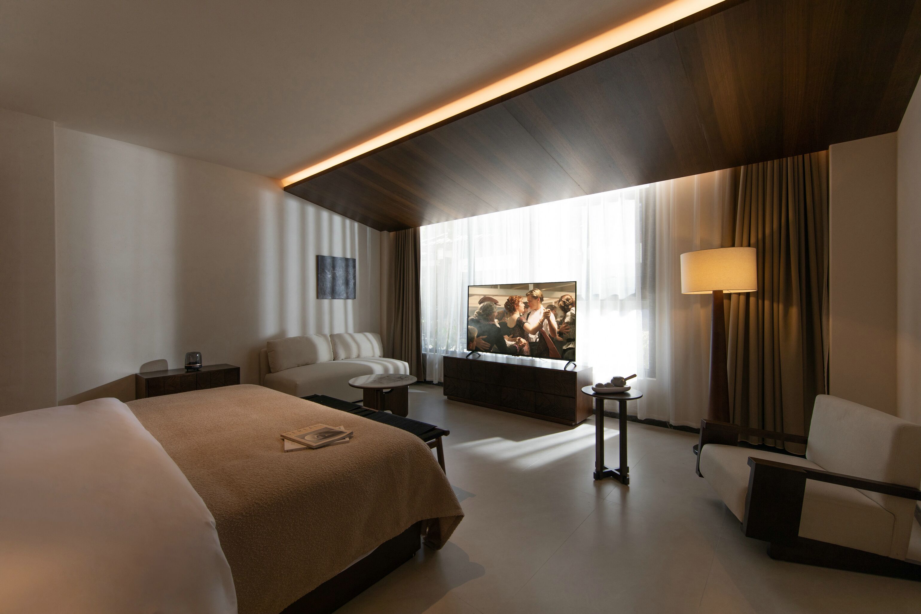A modern hotel room with a large bed, a sofa, a TV, and a lamp.