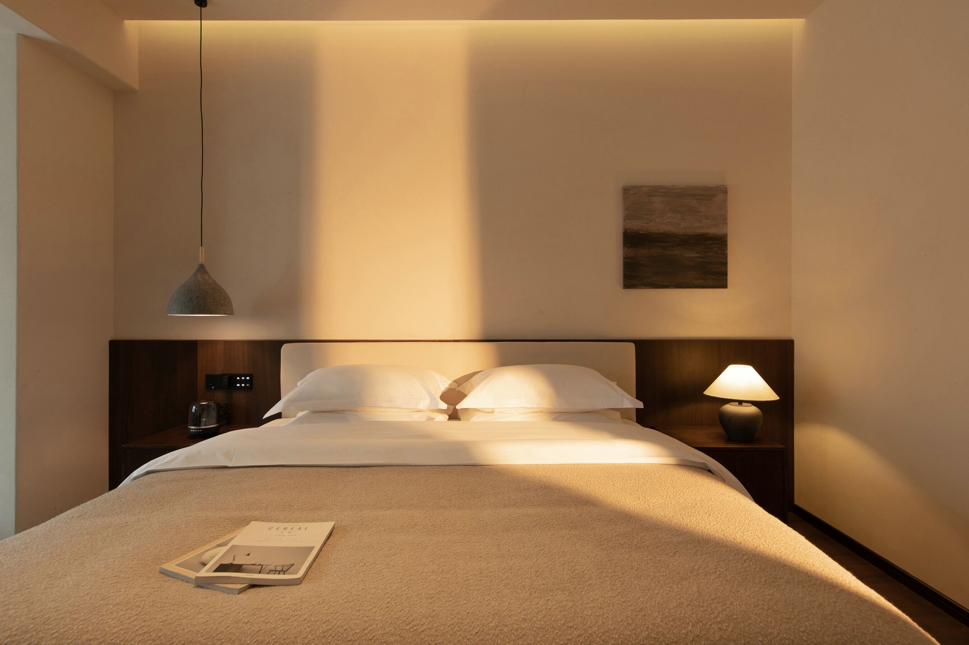 A neatly made bed with white linens, a bedside lamp, and a small table with a glass.