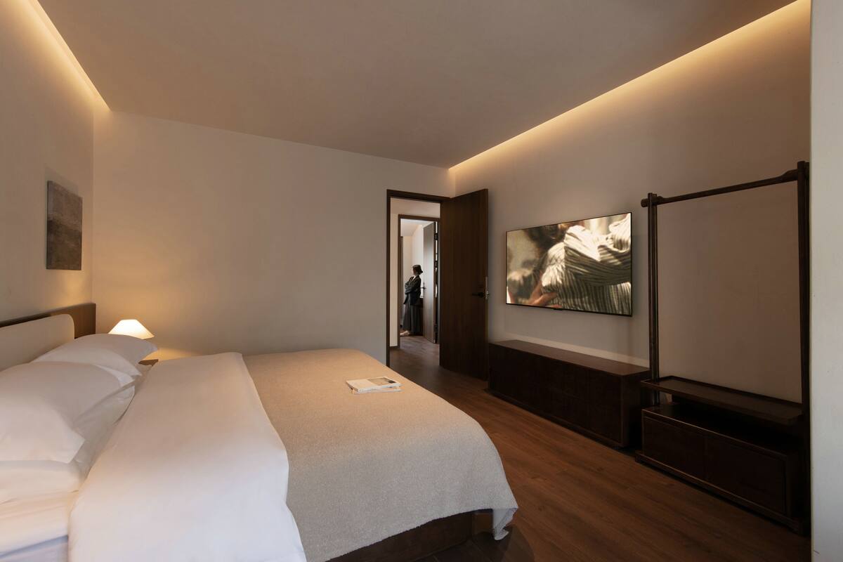 Una habitación de hotel moderna con una cama grande, un televisor de pantalla plana y un banco de madera.