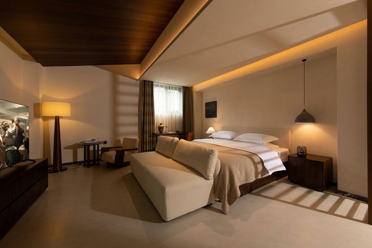 Una habitación de hotel moderna con sofá, cama, televisión, lámpara y mesita de noche.