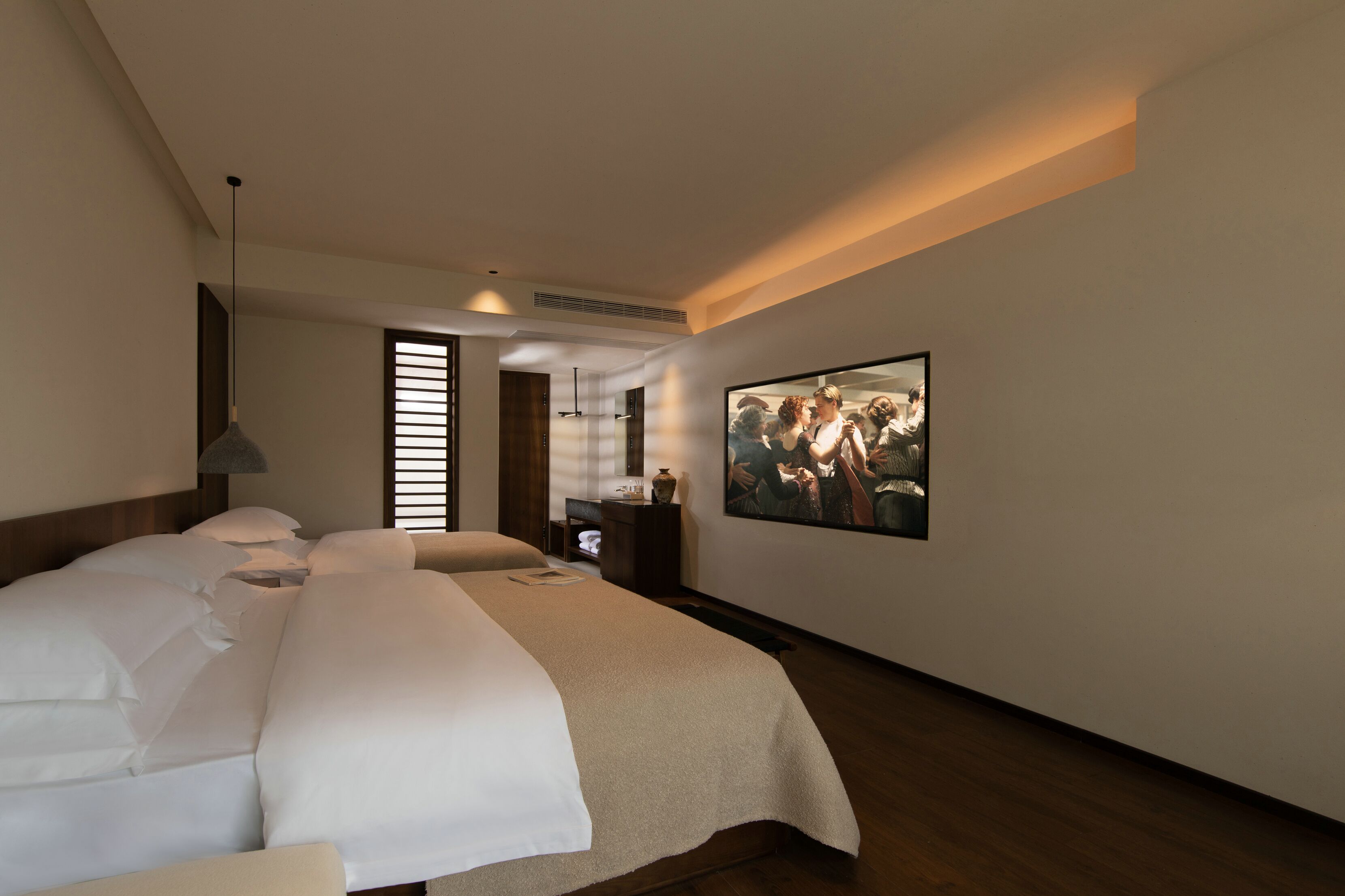 Una habitación de hotel con una cama grande, una mesita de noche, un televisor de pared y una ventana con persianas.