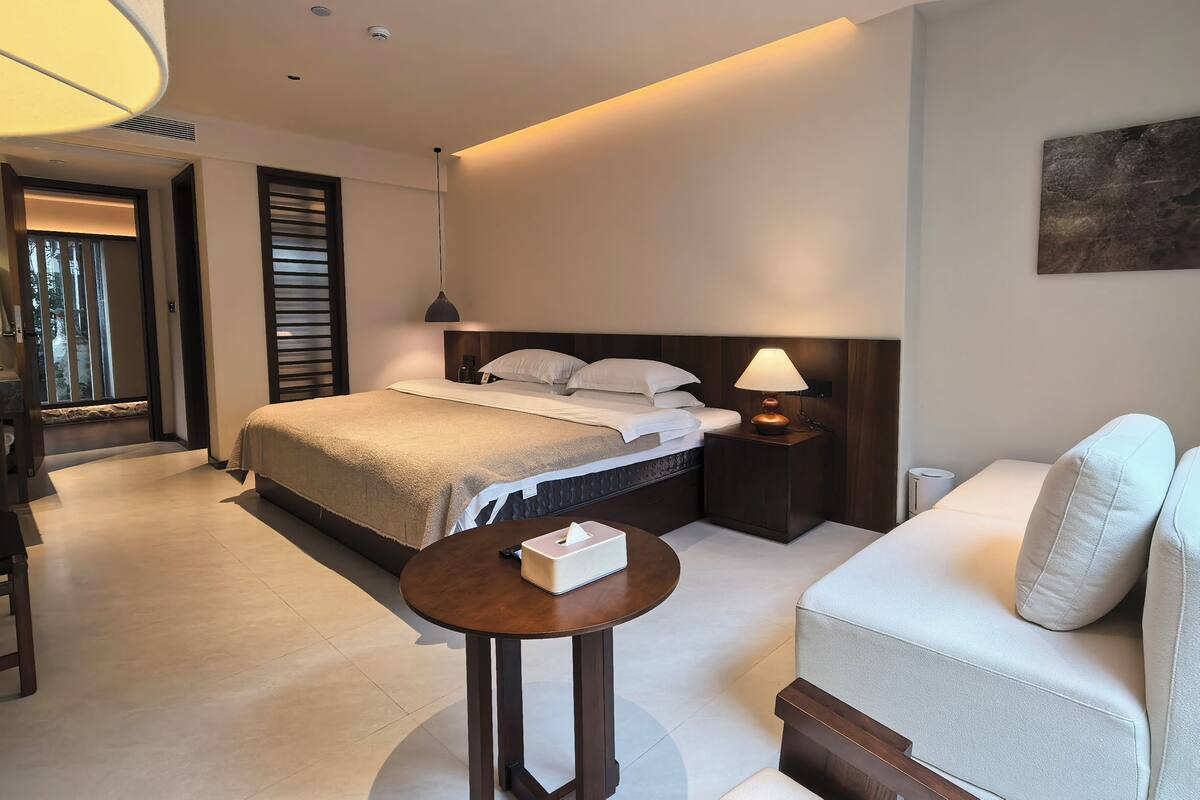 Una habitación de hotel moderna con cama, mesita de noche, lámpara y sofá.