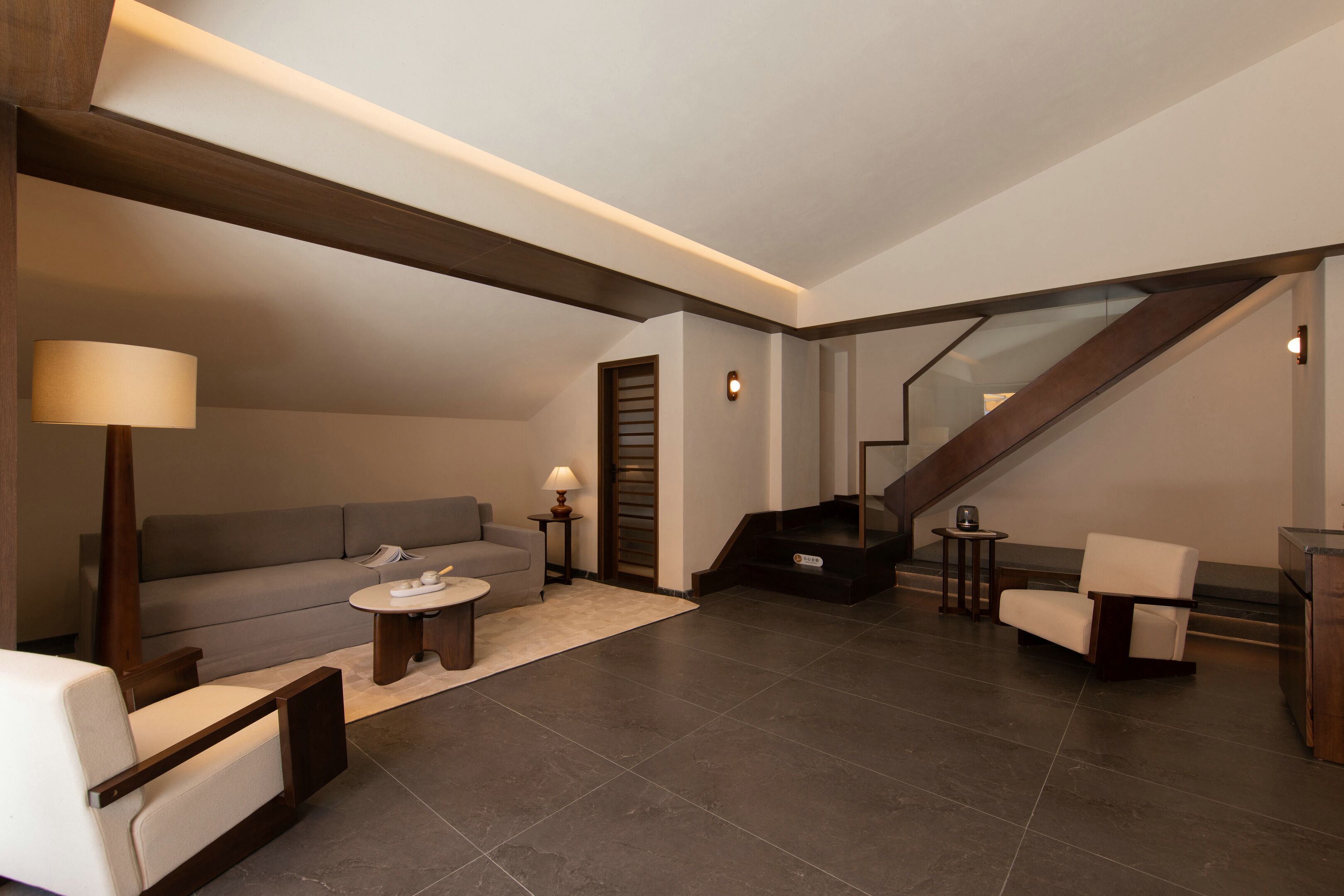 A modern living room with a sofa, armchairs, a coffee table, and a staircase.