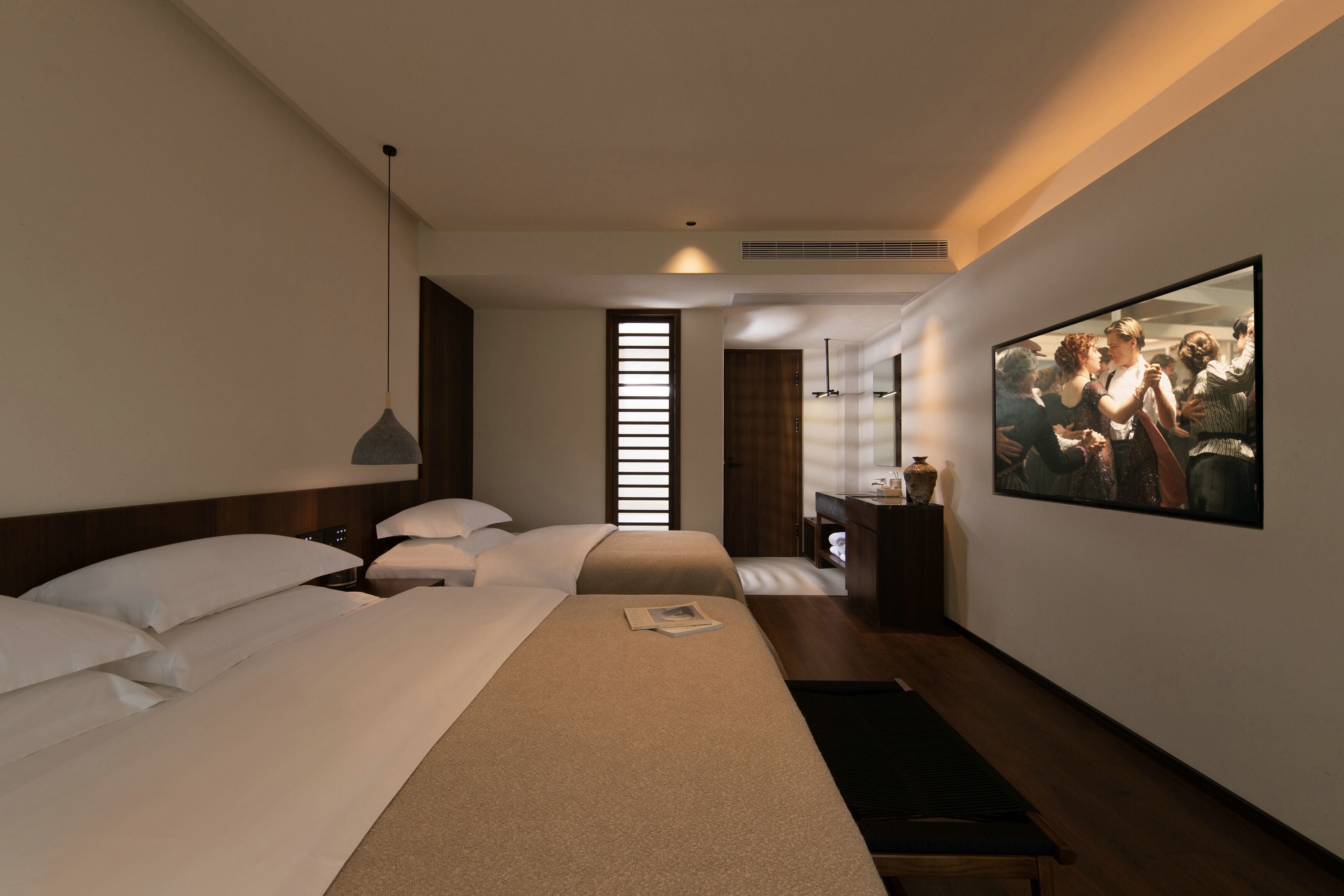 A modern hotel room with a large bed, a bedside table, a small desk, and a large painting on the wall.