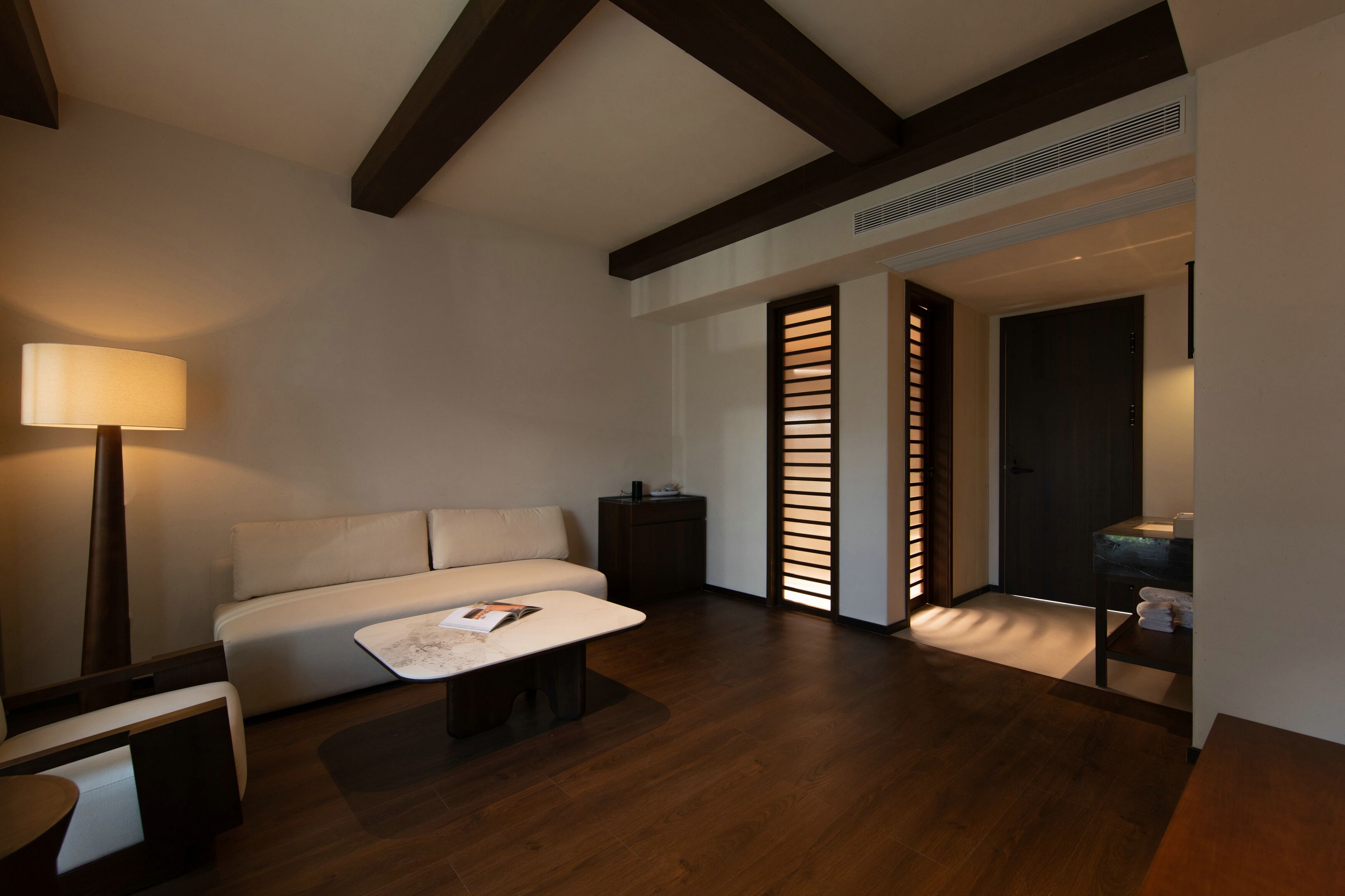Una sala moderna con sofá, mesa de centro y lámpara. Hay una puerta que conduce a otra habitación.