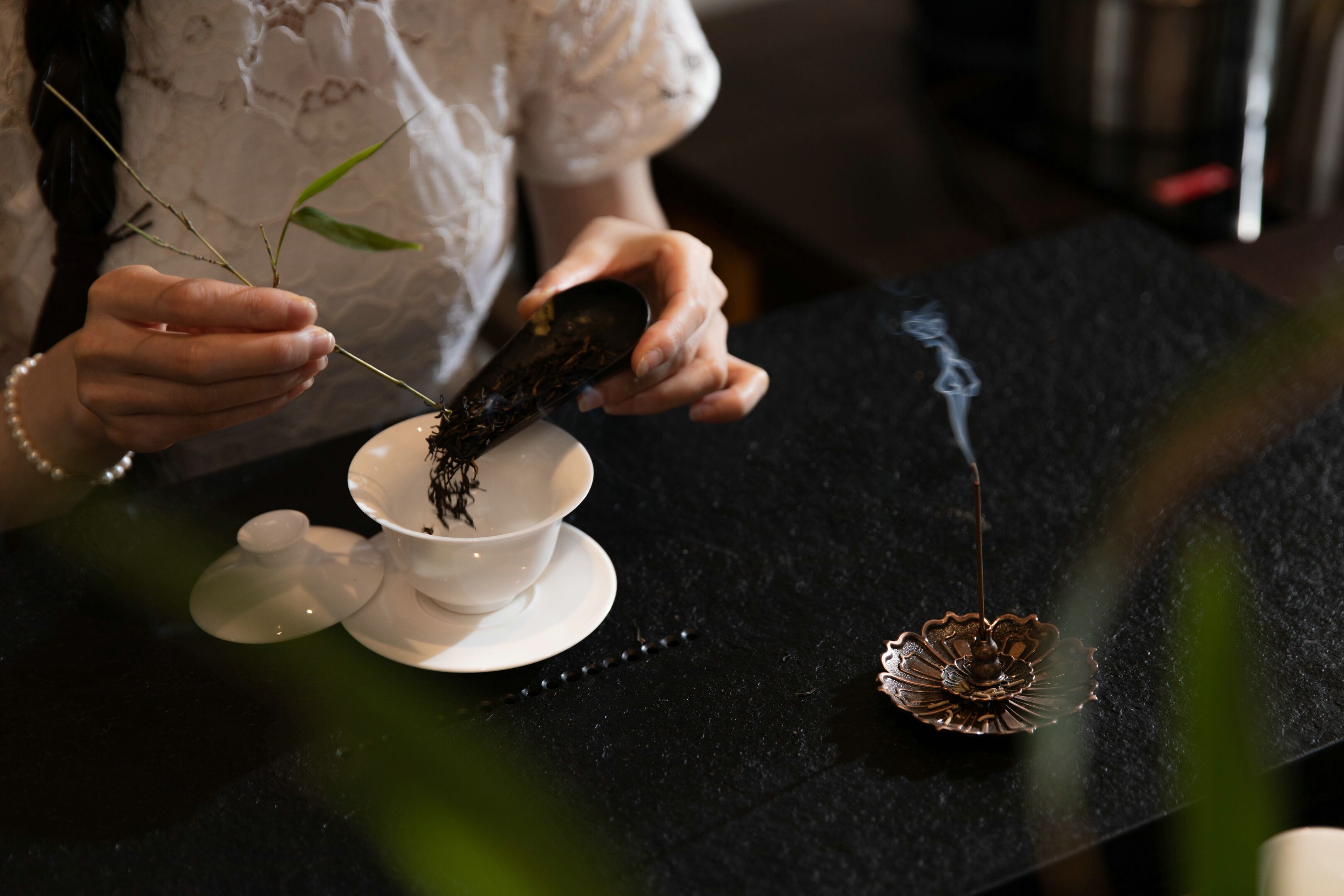A person holding a cup with a plant branch, a small bowl, and a decorative item on a table.