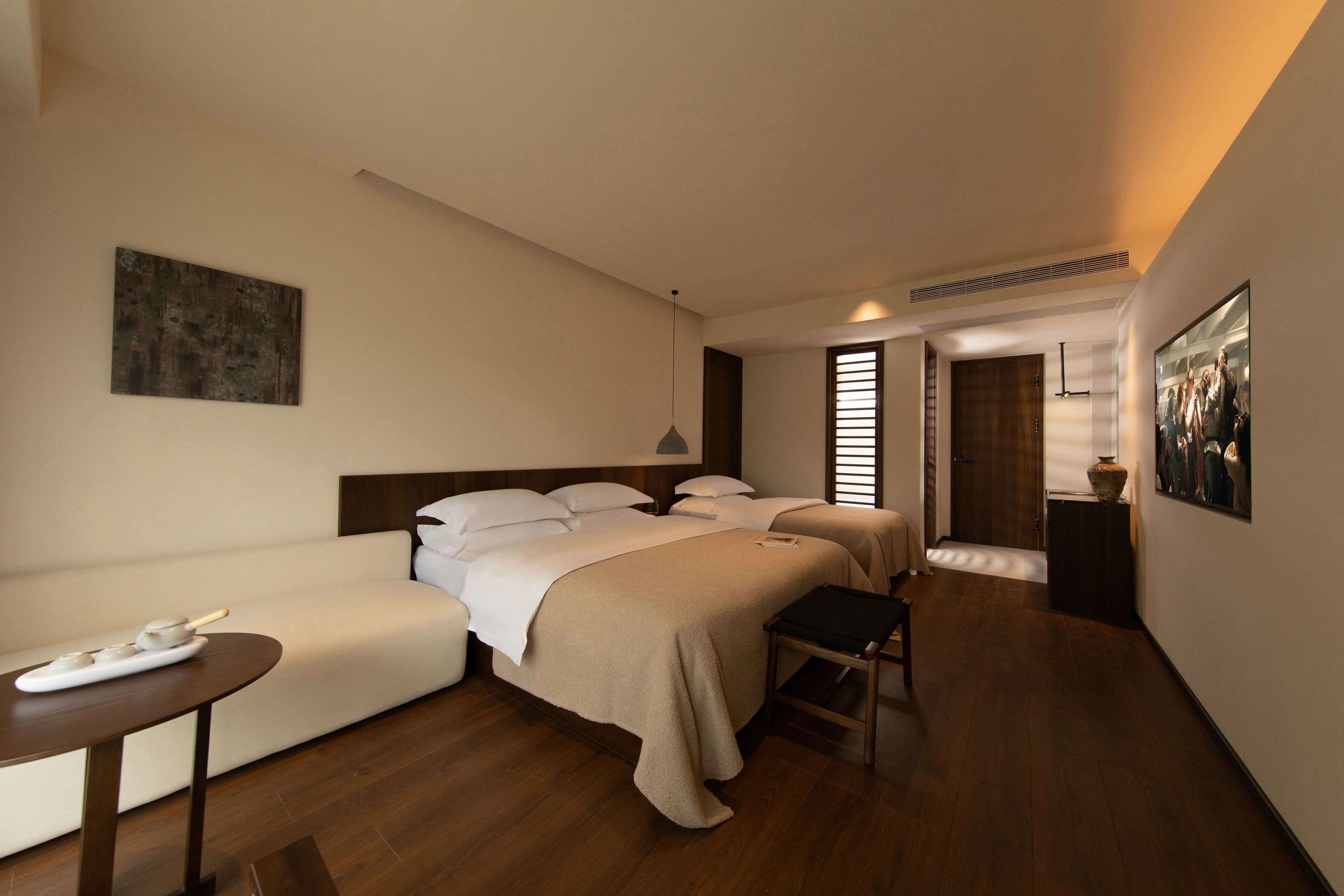 A hotel room with two beds, a sofa, a small table, and a painting on the wall.
