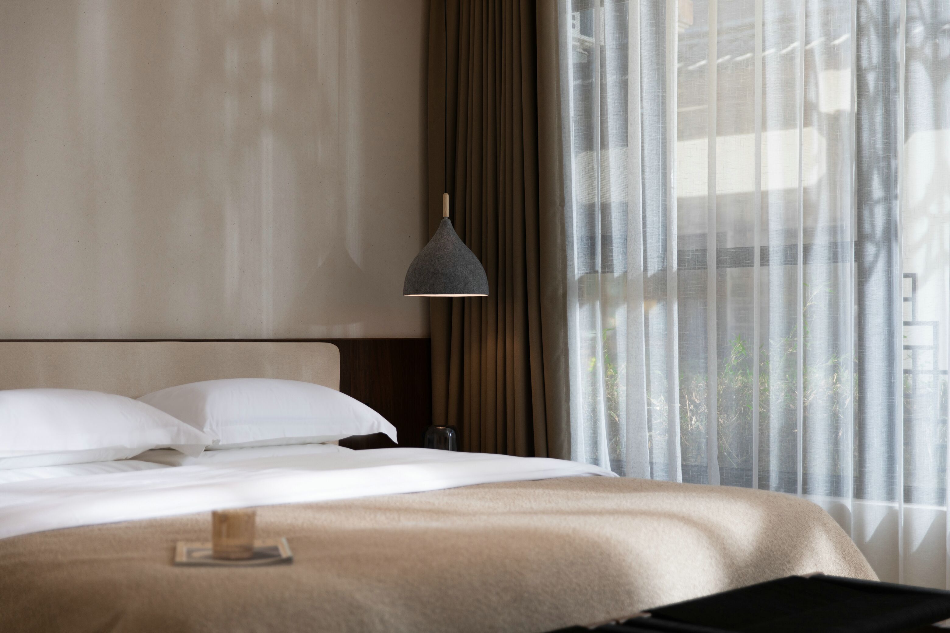 A hotel room with a bed, a bedside table, a lamp, and a window with curtains.