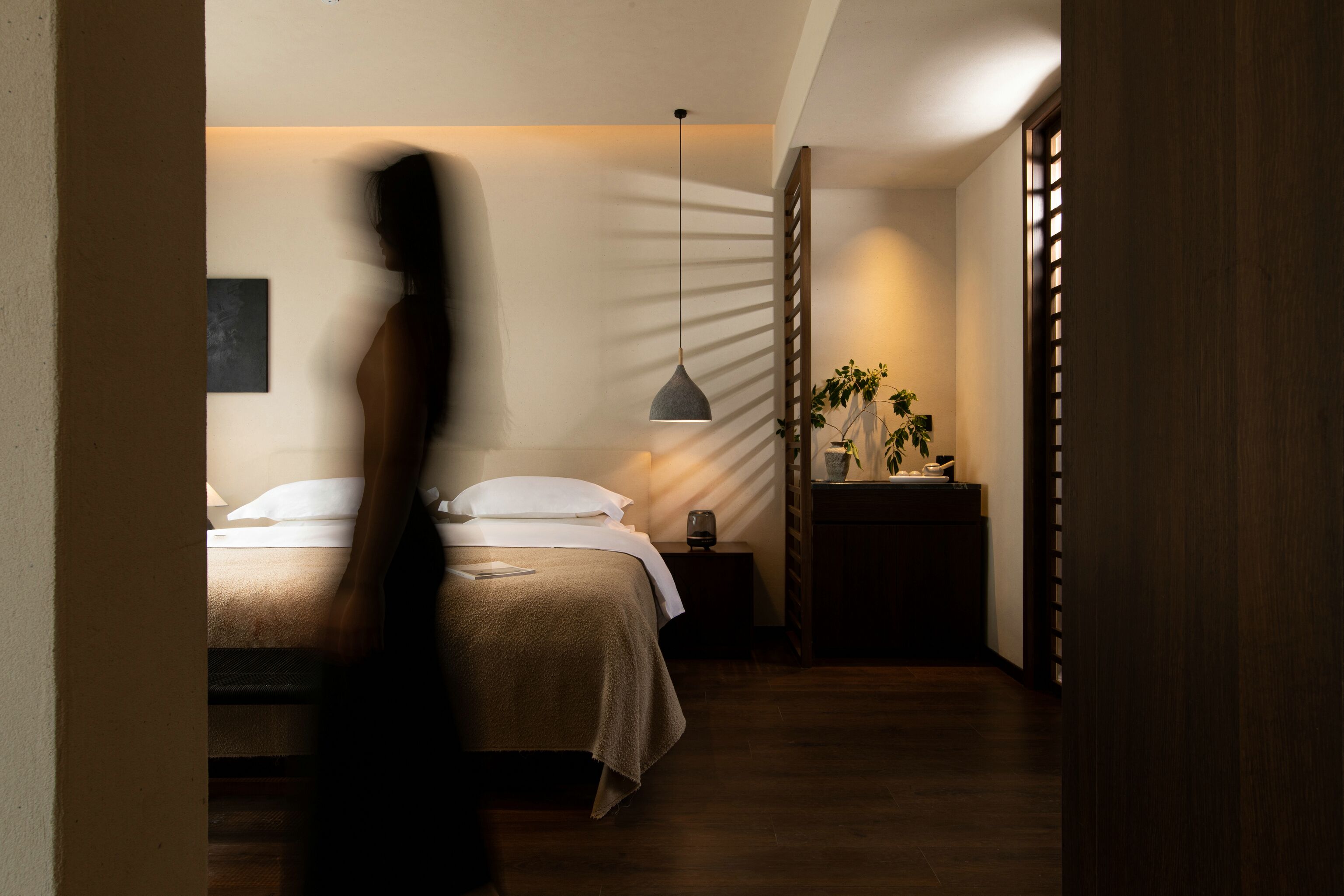A bedroom with a bed, bedside table, lamp, and a plant.