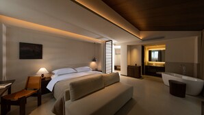 Habitación de hotel moderna con una cama grande, un escritorio, una silla, un sofá, un baño con bañera y un espejo.