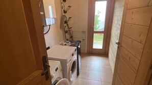 Une buanderie équipée d’un lave-linge et d’un sèche-linge, avec des murs en bois et une porte donnant sur un espace lumineux.