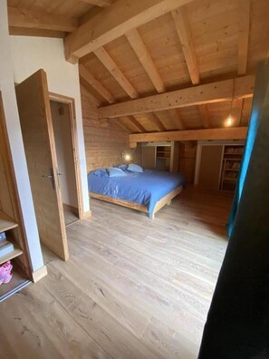 Un dormitorio con techo de madera, una cama con ropa de cama azul y suelo de madera.