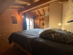 Un dormitorio de cabaña de madera con una cama, una mesita de noche y un ventanal con cortinas.