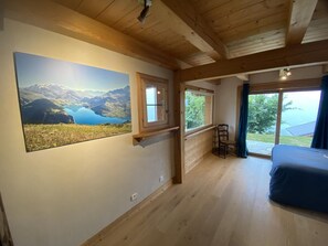 A room with a bed, a window with a view of greenery, and a large landscape painting on the wall. - CHALET HAUT 6 - HAUTELUCE LES SAISIES (HAUTELUCE LES SAISIES)
