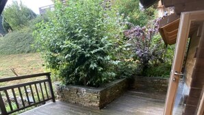 Une terrasse en bois avec un jardinier en pierre et une porte vitrée donnant accès à un bâtiment.