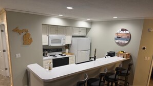 Una cocina moderna con una isla central, taburetes de bar, un microondas, refrigerador y un reloj decorativo en la pared.