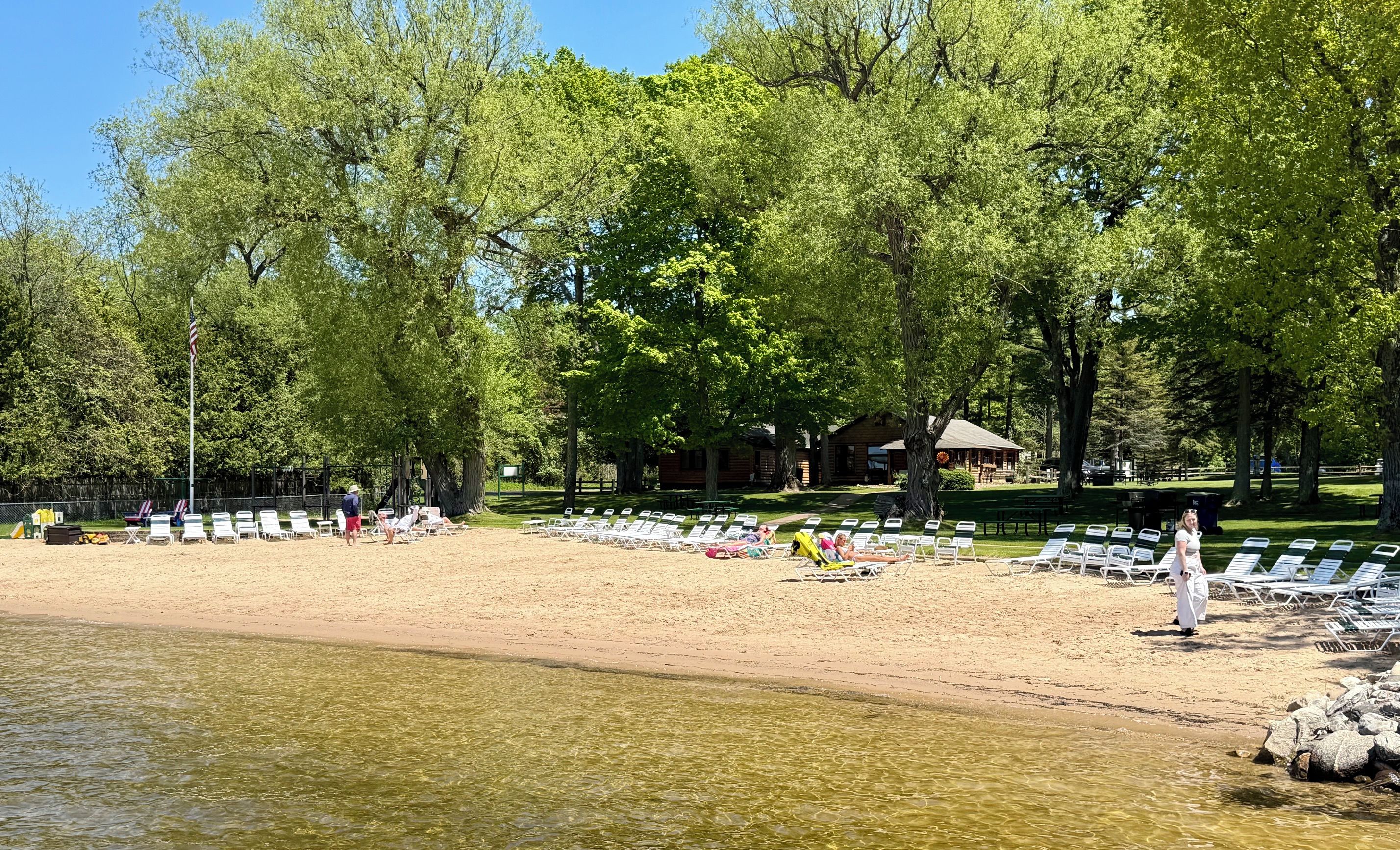 A beach with clear water, lounge chairs, and a cabin in the background.