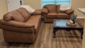 A living room with two brown leather sofas, a glass coffee table, and a door with a window. - Welcoming 6-bedroom house with country living in the shadow of Kyle Field (College Station)