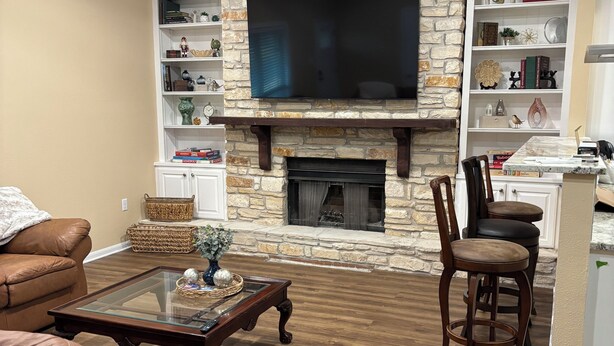 A living room with a stone fireplace, leather sofas, a coffee table, and a TV mounted above the fireplace. - Welcoming 6-bedroom house with country living in the shadow of Kyle Field (College Station)