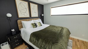 Ein Schlafzimmer mit einem Bett, einem Nachttisch, einer Wandleuchte und abstrakter Kunst.