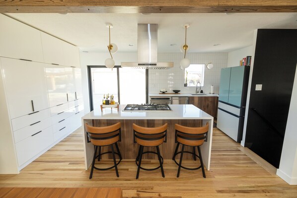 A modern kitchen with white cabinets, a central island with stools, stainless steel appliances, and pendant lighting.